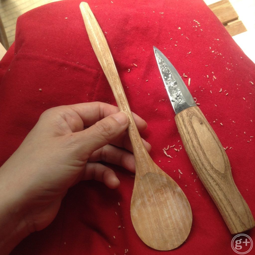 ヤマザクラ材の明るい茶色の食事用スプーンを木の柄のついた手づくりナイフで削っているところ
