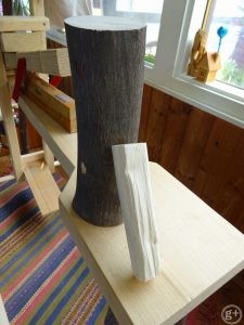 樹皮のついたエゴノキの若木の幹を切ったものと、同じ木を割ってはつったあとの小さめの材が削り馬の上に置いてあるところ