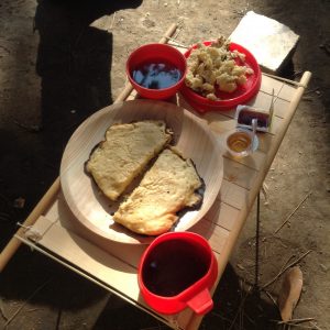 焚火でやいたパンケーキとへびパン、コーヒーを自作の木製キャンプテーブルの上に並べたところ